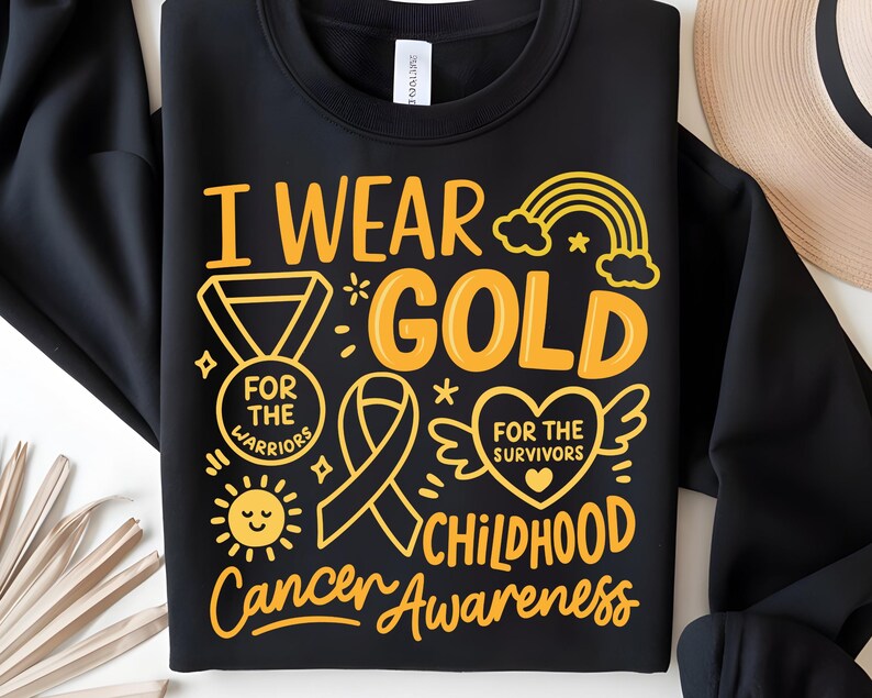 May include: Black sweatshirt with the text "I Wear Gold" in yellow, along with a ribbon, rainbow, and sun graphic. The text also includes "For the Warriors" and "Childhood Cancer Awareness."