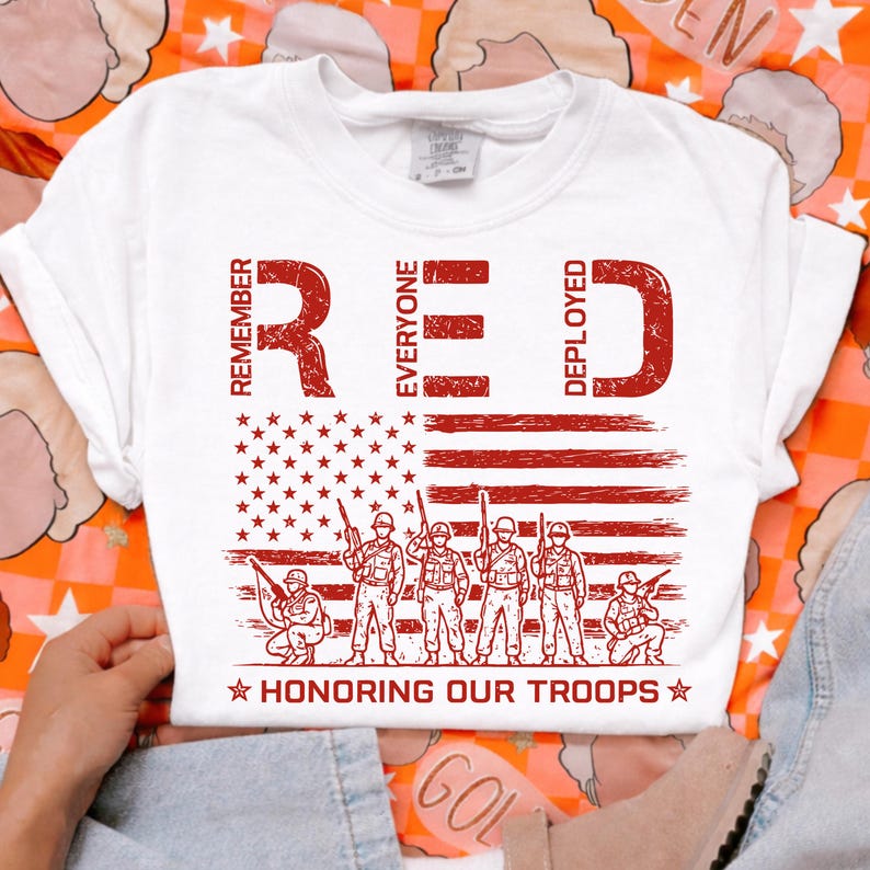 K&ouml;nnte beinhalten: Wei&szlig;es T-Shirt mit roter Grafik. Die Grafik zeigt das Wort "RED" mit den Worten "Remember Everyone Deployed", eine amerikanische Flagge, Soldaten und den Text "Honoring Our Troops."