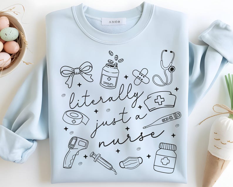 May include: Light blue sweatshirt with the text "literally just a nurse" and medical-themed illustrations in black. The design includes a bow, pills, bandages, a stethoscope, a nurse's hat, a thermometer, a medical mask, a syringe, and a bottle of pills.