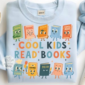 Puede incluir: Sudadera azul claro con un gráfico colorido de libros animados. Los libros están etiquetados con géneros como "Drama", "Romance" y "Detective". También aparece el texto "COOL KIDS READ BOOKS". La sudadera tiene la etiqueta "amor".