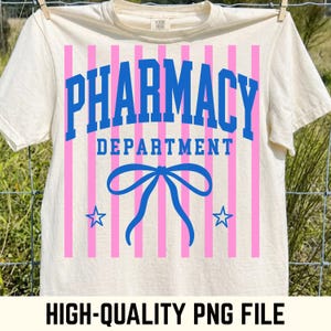 May include: A cream-colored t-shirt featuring a graphic design with vertical pink stripes. The text PHARMACY DEPARTMENT is printed in blue, arched above a blue bow illustration, flanked by two blue stars on a light-colored fabric background.