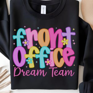 Puede incluir: Sudadera negra con cuello redondo con las palabras "Front Office Dream Team" en letras coloridas y de estilo burbuja. El diseño incluye flores y estrellas en tonos rosa, naranja, amarillo y azul. Un diseño casual y divertido para un equipo.