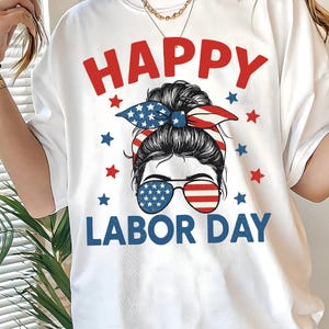 Könnte beinhalten: Weißes T-Shirt mit einem Grafikdesign zum Tag der Arbeit. Das Design zeigt den Text "HAPPY LABOR DAY" in Rot und Blau, zusammen mit dem Gesicht einer Frau, die eine Sonnenbrille und ein patriotisches Stirnband trägt. Rote und blaue Sterne sind um das Design herum verteilt.