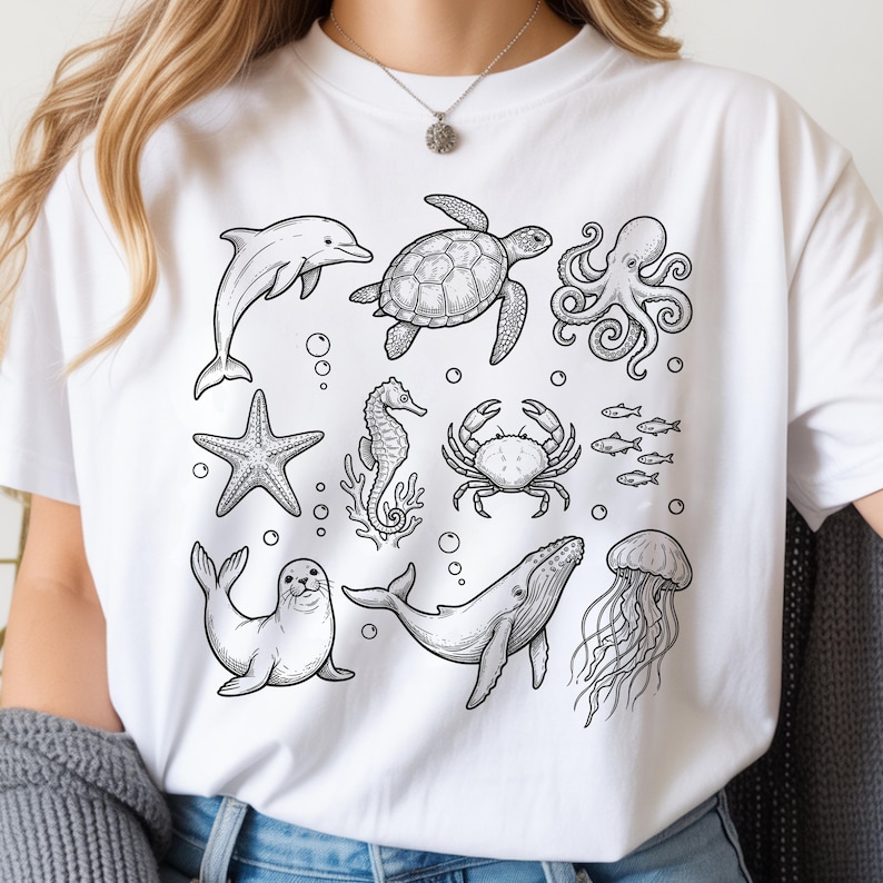 May include: White t-shirt featuring a black and white illustration of various sea creatures, including a dolphin, turtle, octopus, starfish, seahorse, crab, fish, seal, whale, and jellyfish. The design is a detailed line drawing.