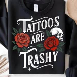 May include: Black sweatshirt with the text "Tattoos Are Trashy" in white script, featuring red roses and a skull graphic. The roses have green leaves, and the design is centered on the front.