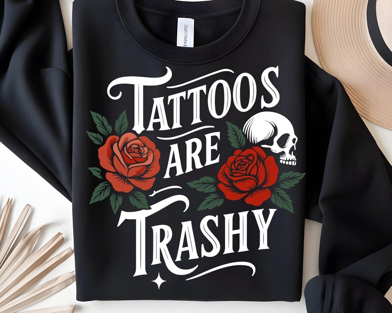 May include: Black sweatshirt with the text "Tattoos Are Trashy" in white script, featuring red roses and a skull graphic. The roses have green leaves, and the design is centered on the front.
