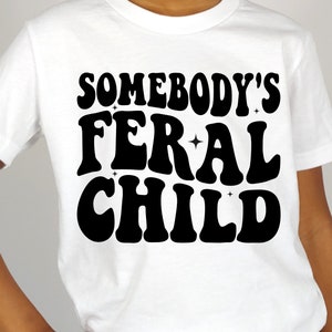 May include: White t-shirt with black text that reads "Somebody's Feral Child" in a retro font.