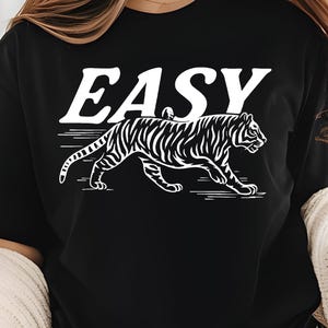 May include: Black t-shirt with the word "EASY" in white block letters above a white tiger illustration. The tiger is walking with its stripes visible.