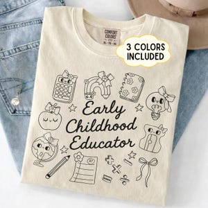 May include: Cream-colored t-shirt with a black graphic design featuring school-themed illustrations and the text "Early Childhood Educator." The design includes a calculator, rainbow, apple, and other elements.