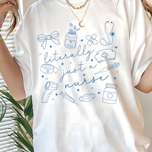 May include: White t-shirt with a blue illustration of medical supplies and the text "literally just a nurse". The design includes a bow, medicine bottles, bandages, a stethoscope, a nurse's hat, a thermometer, and a syringe.