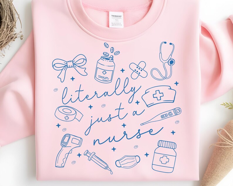 May include: A light pink sweatshirt with a blue graphic design. The design includes medical symbols such as a stethoscope, pills, and a nurse's hat, along with the text "literally just a nurse".