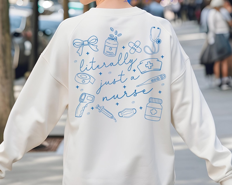 May include: Cream-colored sweatshirt with blue illustrations of medical tools and the phrase "literally just a nurse." The design includes a stethoscope, pills, bandages, and a thermometer. A casual, comfortable top for healthcare professionals.