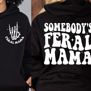 May include: Black hoodie with a white graphic on the front that says "Feral Mama" with a skeleton hand making the rock and roll sign. The back of the hoodie has a white graphic that says "Somebody's Feral Mama".