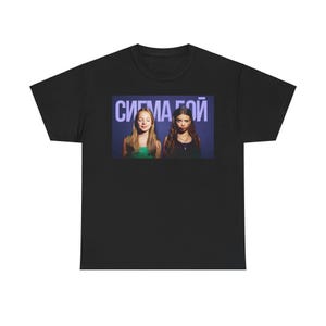 Könnte beinhalten: Ein schwarzes Kurzarm-T-Shirt mit einem rechteckigen Grafikdruck auf der Brust. Der Druck zeigt zwei Personen vor einem dunkelblauen Hintergrund mit dem kyrillischen Text "СИГМА БОЙ" in großen weißen Buchstaben über ihren Köpfen.