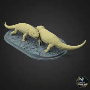 Könnte beinhalten: Zwei hellbeige Dinosaurierfiguren auf einer grauen, oval geformten Basis. Die Dinosaurier sind so positioniert, als würden sie interagieren, mit detaillierten Hautstrukturen. Die Basis hat ein strukturiertes, felsiges Aussehen, und der Hintergrund ist einfarbig dunkelgrau.