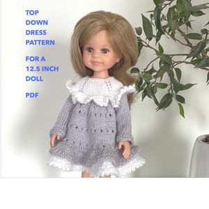 Può includere: Una bambola con un vestito lavorato a maglia grigio e bianco. L'abito ha un colletto in pizzo bianco e un bordo in pizzo bianco sull'orlo. Il testo sull'immagine recita: "TOP DOWN DRESS PATTERN FOR A 31.75 cm DOLL PDF."