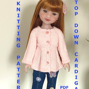 May include: A doll wearing a light pink knitted cardigan with three buttons, paired with blue jeans featuring floral and butterfly embellishments. The text "KNITTING PATTERN" and "TOP DOWN CARDIGAN" are displayed vertically. The word "PDF" is also visible.