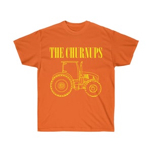 Puede incluir: Camiseta naranja con el texto "THE CHURNUPS" en letras amarillas sobre un contorno amarillo de un tractor. El tractor tiene neum&aacute;ticos traseros grandes y un dise&ntilde;o detallado.