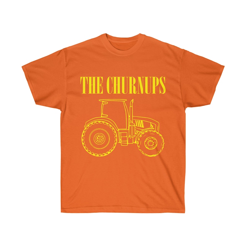 Puede incluir: Camiseta naranja con el texto "THE CHURNUPS" en letras amarillas sobre un contorno amarillo de un tractor. El tractor tiene neum&aacute;ticos traseros grandes y un dise&ntilde;o detallado.