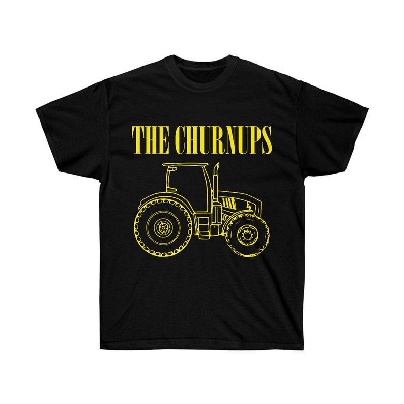 Puede incluir: Camiseta negra con un contorno amarillo de un tractor y el texto "THE CHURNUPS" encima. El dise&ntilde;o del tractor incluye ruedas grandes, una cabina y un tubo de escape. La camiseta es de un material suave.