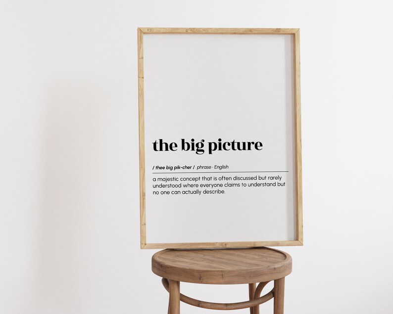 Op de afbeelding: Een ingelijst print met een witte achtergrond en zwarte tekst. De tekst definieert de zin "het grote plaatje" als een "majestueus concept dat vaak wordt besproken maar zelden wordt begrepen, waar iedereen beweert het te begrijpen, maar niemand het echt kan beschrijven."