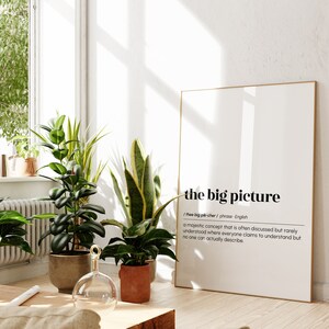 Op de afbeelding: Een ingelijst print met een witte achtergrond en zwarte tekst die "the big picture" en de definitie ervan weergeeft. De print hangt aan een witte muur in een kamer met planten.