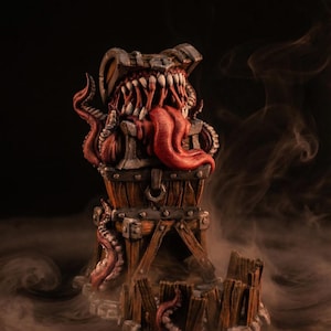 Może przedstawiać: Szczegółowa rzeźba fantasy przedstawiająca skrzynię ze skarbami z potwornymi ustami i mackami. Skrzynia jest brązowa z metalowymi akcentami, a pysk stworzenia jest wypełniony ostrymi zębami i długim czerwonym językiem. Rzeźba stoi na drewnianej podstawie.