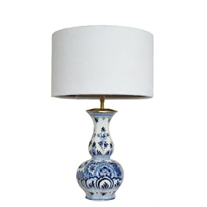 Peut inclure: Une lampe de table en céramique blanche avec un motif floral bleu et blanc. La lampe a un abat-jour en tissu blanc.
