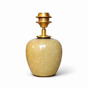 Peut inclure: Un pied de lampe décoratif avec une finition craquelée dans des tons de jaune et de beige. La lampe est dotée d'une quincaillerie de couleur laiton en haut et à la base, conçue pour accueillir un abat-jour. La base a une forme arrondie, semblable à un vase.