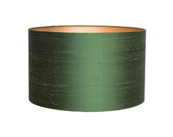 May include: A cylindrical lampshade with a dark green, textured exterior. The interior rim has a warm, copper-colored finish. The lampshade is a solid color and has a smooth, slightly reflective surface.
