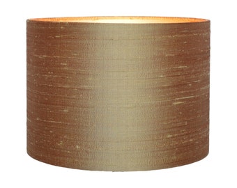 May include: A cylindrical lamp shade featuring a textured, metallic bronze-toned fabric finish with horizontal striations. The shade has an open top and bottom, revealing a light interior lining that glows when illuminated from within.