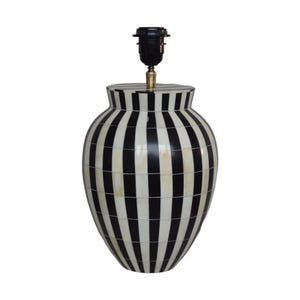 Puede incluir: Una base de lámpara decorativa con un patrón de rayas blancas y negras. La lámpara tiene un portalámparas en la parte superior y un acento metálico dorado. La base tiene forma de jarrón y las rayas son verticales.