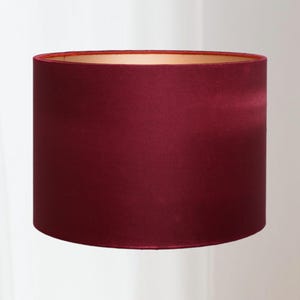 Può includere: Paralume cilindrico di colore bordeaux scuro. Il paralume ha una consistenza liscia, simile al raso, e un interno color oro a contrasto. I bordi superiore e inferiore sono arrotondati. Il paralume è progettato per diffondere la luce.