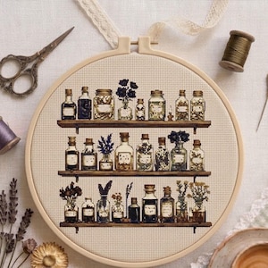 May include: A circular wooden embroidery hoop containing a cross-stitch pattern of three shelves filled with various glass apothecary bottles, jars, and vases containing dried flowers, herbs, and liquids, displayed on a light-colored fabric.