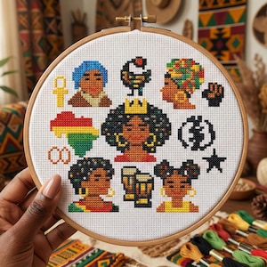 May include: A cross-stitch embroidery hoop featuring various Black culture icons. The design includes portraits, symbols, and the African continent in red, yellow, green, and black. The hoop is held by a hand, with colorful embroidery floss in the background.