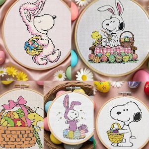 May include: A selection of cross-stitch embroidery hoops with Easter designs. The hoops depict Snoopy and other characters dressed as bunnies, carrying baskets of Easter eggs. The colour scheme includes pastels and bright colours, with floral and egg accents.