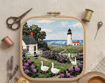May include: A cross-stitch embroidery project in a wooden hoop featuring a coastal scene with a white lighthouse, a cottage, a white picket fence, and three white geese in a garden of purple flowers, accompanied by scissors, thread, and a needle.