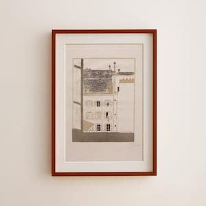 Op de afbeelding: Een ingelijste kunstdruk met een gedetailleerde architecturale illustratie van een gebouw met meerdere ramen en een uitzicht op het dak. Het kunstwerk is in grijstinten en bruin, geplaatst in een witte passe-partout en een donkerbruine houten lijst.