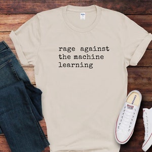 May include: A cream-colored t-shirt with the text "rage against the machine learning" in black. The shirt is paired with blue jeans and white sneakers with red accents. The items are arranged on a wooden surface.