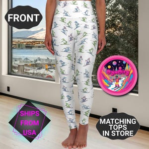 May include: White leggings with a repeating pattern of skiers in blue, green, and purple. The leggings are high-waisted and form-fitting. The image also includes the text "FRONT", "SHIPS FROM USA", and "MATCHING TOPS IN STORE".
