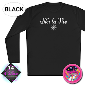 May include: Black long-sleeve shirt with the text "Ski la Vie" in white script and a white snowflake design. A pink and purple sticker with a skier is on the bottom right. The shirt is available in 14 colors.