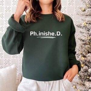 May include: A dark green sweatshirt with the text "Ph.inishe.D." in white lettering.