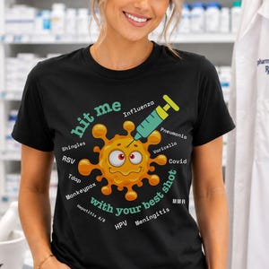 May include: A black t-shirt featuring a central graphic of a yellow, cartoonish virus character being poked by a syringe. The text reads "hit me with your best shot" surrounded by labels for Shingles, RSV, Tdap, Monkeypox, Hepatitis A/B, HPV, Meningitis, MMR, Covid, Varicella, Pneumonia, and Influenza.