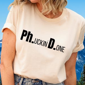 May include: A white t-shirt with the text "Ph.uckin' D.one" printed in black.