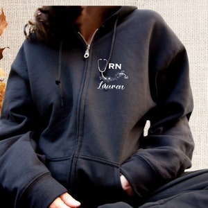 May include: Black zip-up hoodie with a white graphic of a stethoscope and the text "RN Lauren".