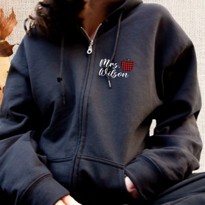 May include: Black zip-up hoodie with a red and black plaid apple and the text "Mrs. Wilson" on the front.