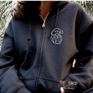 May include: Black zip-up hoodie with a white outline of Santa Claus on the front. The text "Teacher" and "Mrs. Parker" is visible on the bottom of the hoodie.