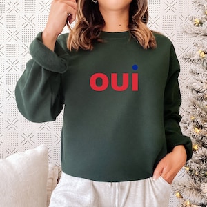 May include: A dark green sweatshirt with a red "oui" graphic and a small blue dot.