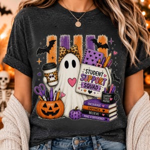Può includere: Una t-shirt grigio scuro mélange con la grafica di un fantasma bianco con un fiocco leopardato, che tiene in mano un caffè ed è accanto a una zucca piena di materiale scolastico. Il testo recita Student Support Squad e Encourage Empower Believe.