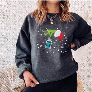 May include: Dark gray sweatshirt featuring a Grinch-themed design. The design includes a green hand holding a bottle labeled "Propofol" with the text "Propofol is the best medicine". A red and white Santa hat is also part of the design, along with snowflakes.